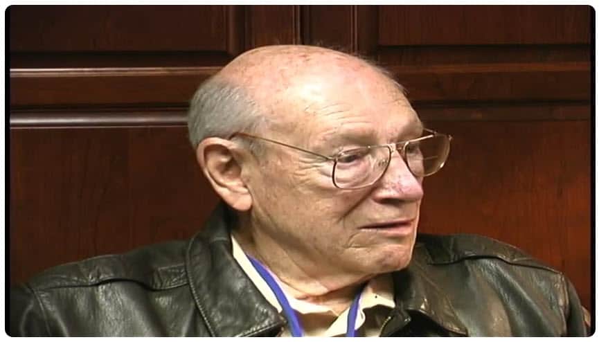 Elderly man wearing glasses and leather jacket, speaking at a book event for Steve Snyder, author of WWII aviation stories.